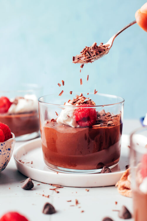 Sprinkling shaved dark chocolate into a jar of pot de creme