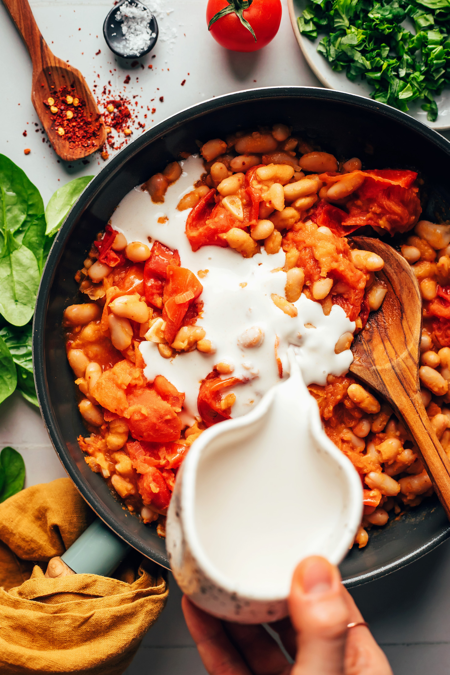 Pouring cashew cream over sautéed veggies and white beans
