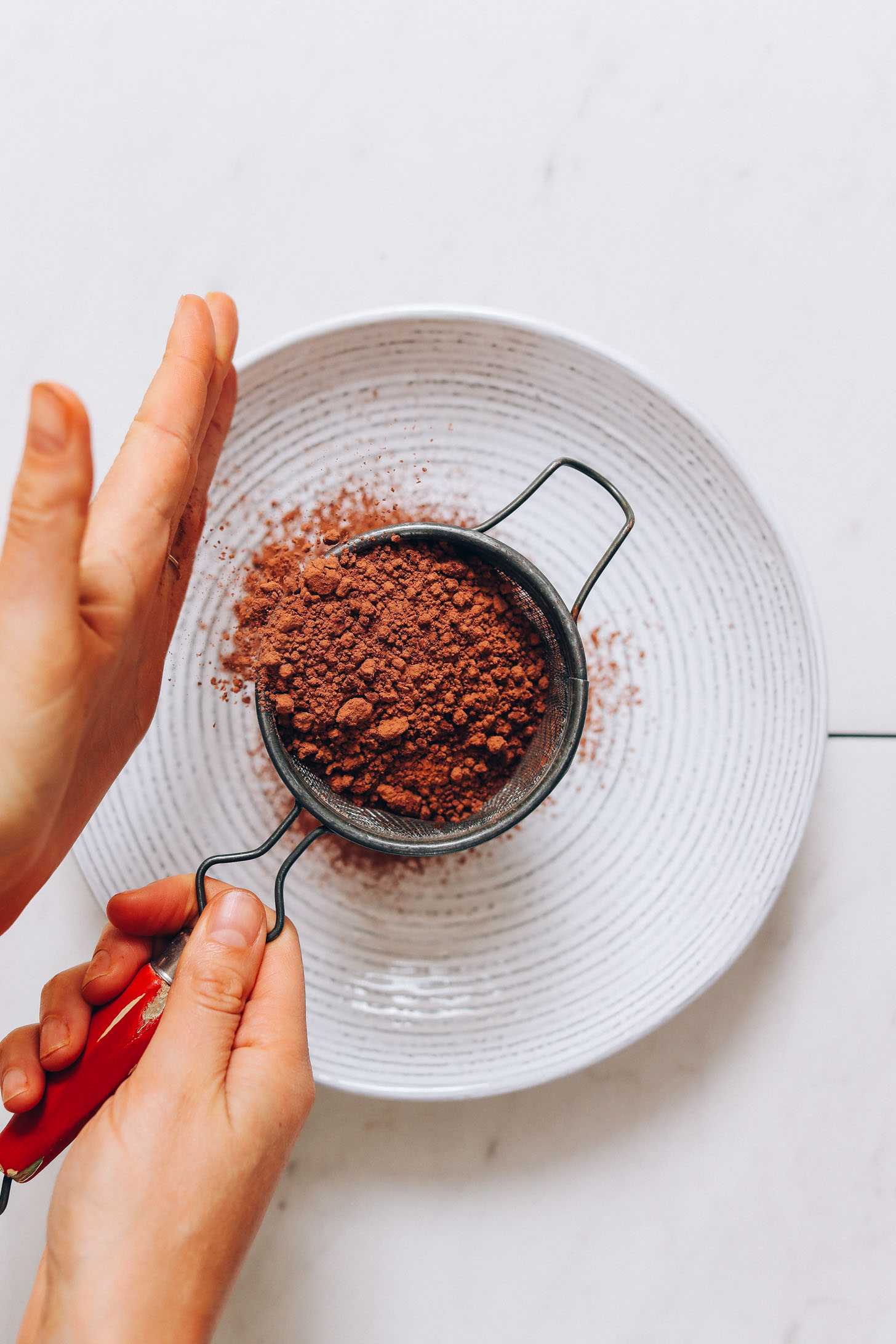 Using a fine mesh strainer to sift cacao powder into a bowl