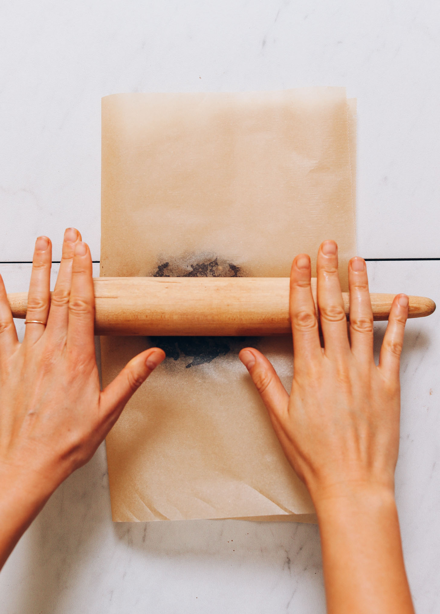 Using a rolling pin over parchment paper to roll Honey-Sweetened Chocolate into bars