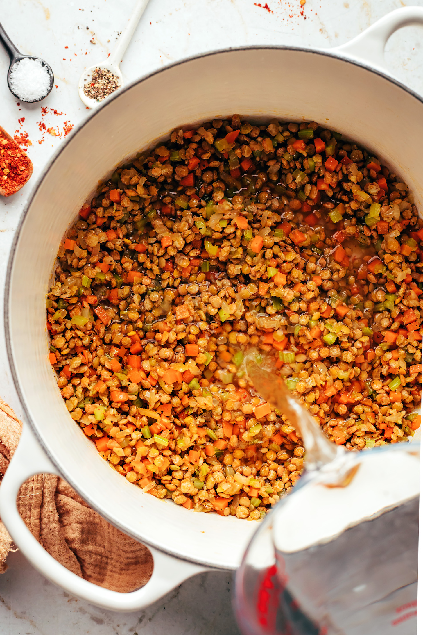 Pouring water over lentils and sautéd veggies in a Dutch oven