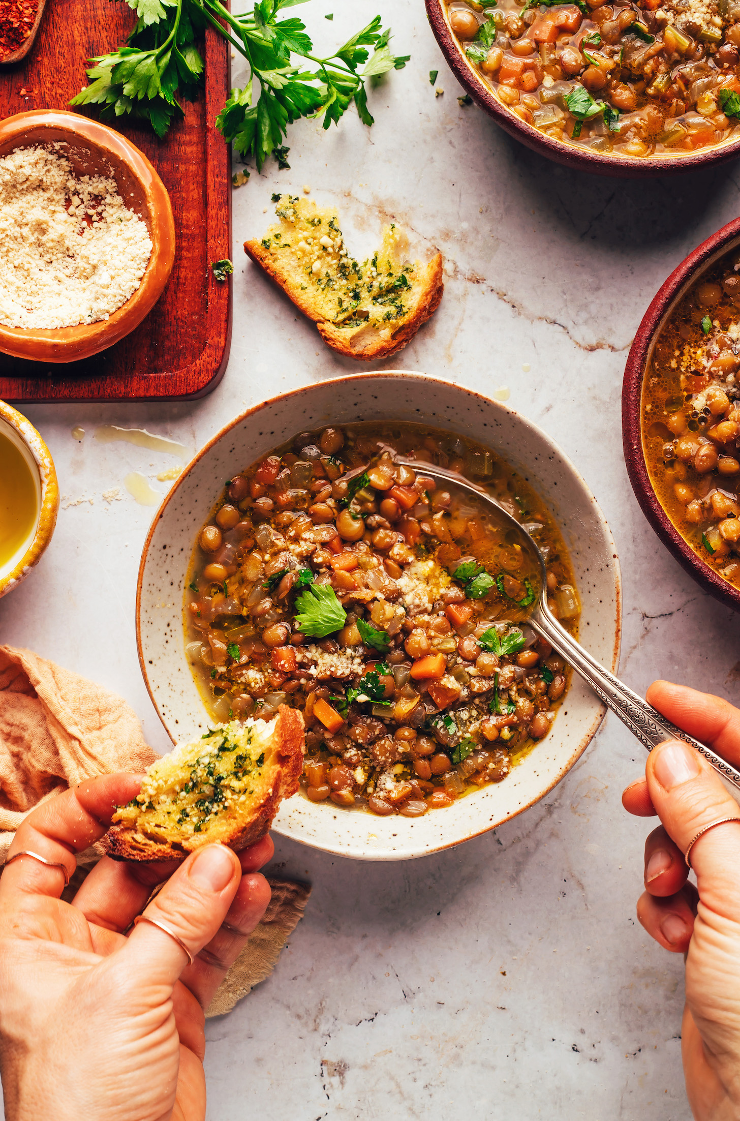 Holding a spoon in a bowl of lentil soup and a piece of garlic bread in the other hand